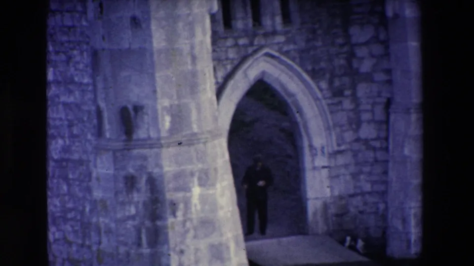 The man remains in the Ireland stone archway, small in frame against pointed masonry and heavy shadow with a cool blue-purple film cast.