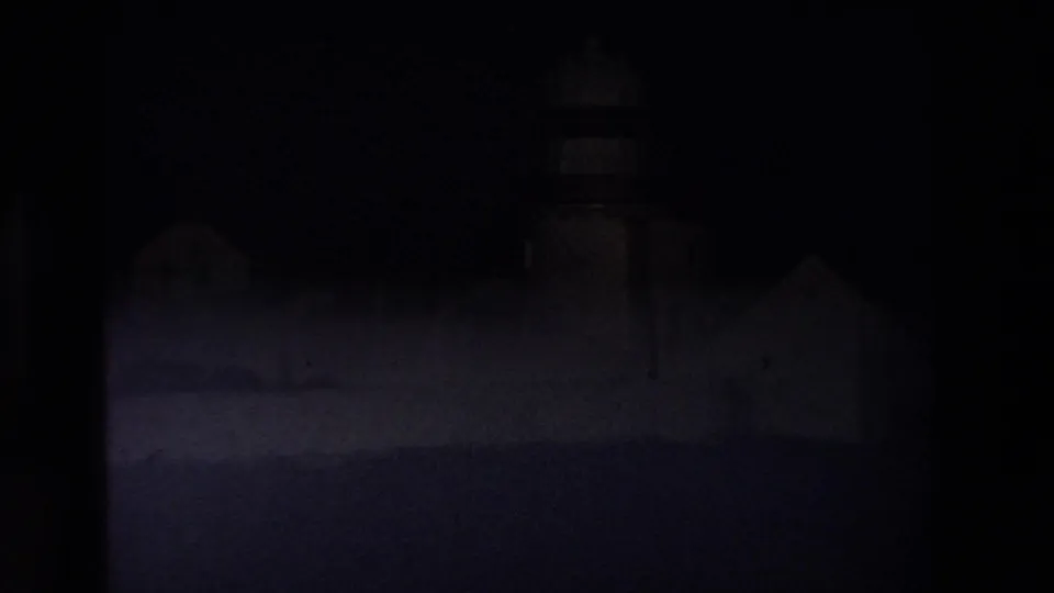 Underexposed 1969 Ireland 8mm frame where the lighthouse and white-walled buildings are barely visible through darkened film exposure.