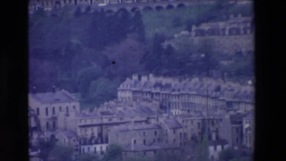 1969 Ireland 8mm frame showing an elevated view of a historic-looking town with rows of stone buildings, trees, and an arched viaduct in the distance.