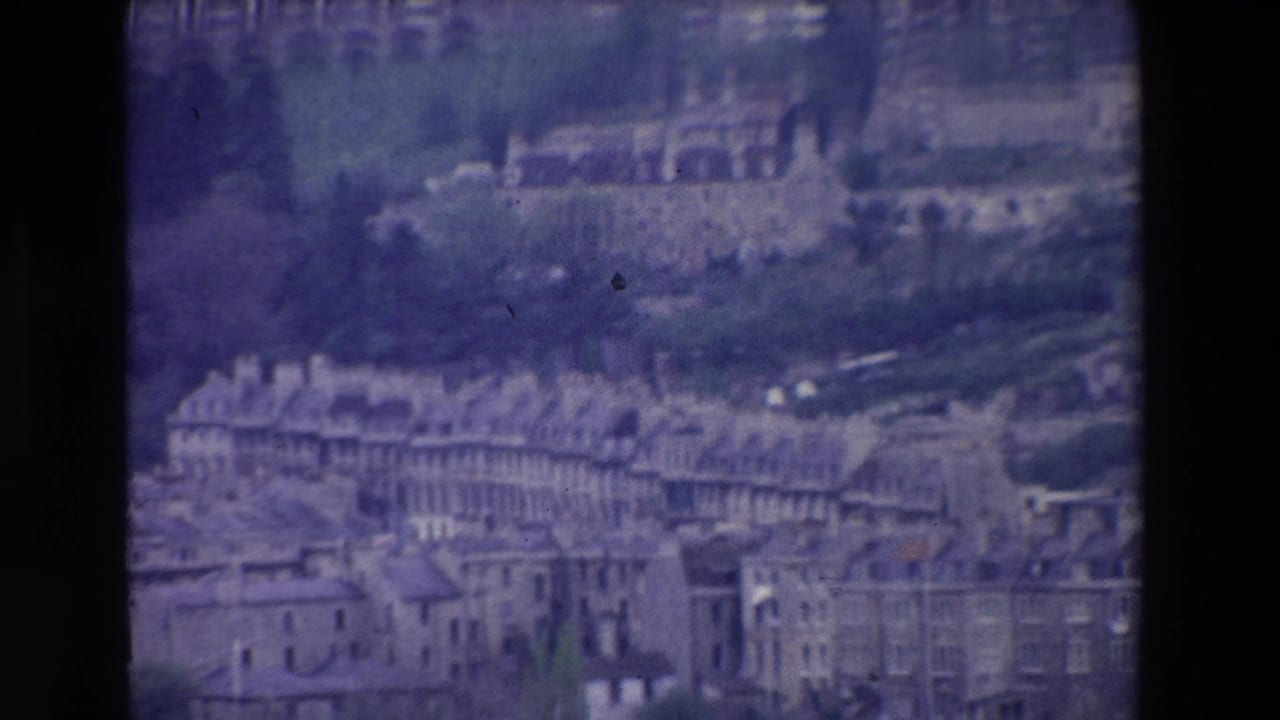 1969 Ireland frame with a visitor-shot elevated view of clustered stone or masonry buildings, slate-like roofs, hillside greenery, and arched structures in the distance.