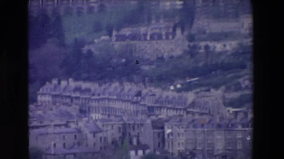 1969 Ireland frame with a visitor-shot elevated view of clustered stone or masonry buildings, slate-like roofs, hillside greenery, and arched structures in the distance.