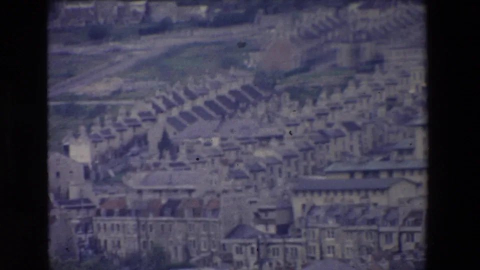 1969 Ireland home-movie frame with a soft panoramic view across dense town rooftops, hillside streets, and a prominent church spire.
