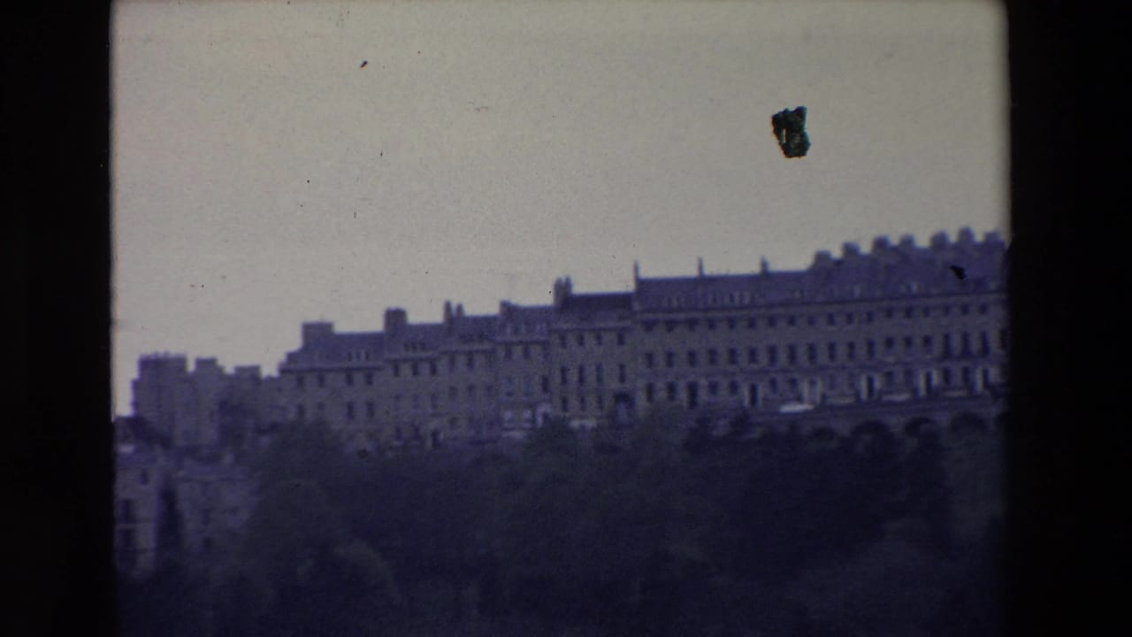 1969 Ireland home-movie frame showing a distant grand stone building range across a hillside, with trees in the foreground and visible 8mm frame edges.