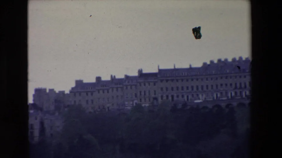 1969 Ireland home-movie frame showing a distant grand stone building range across a hillside, with trees in the foreground and visible 8mm frame edges.