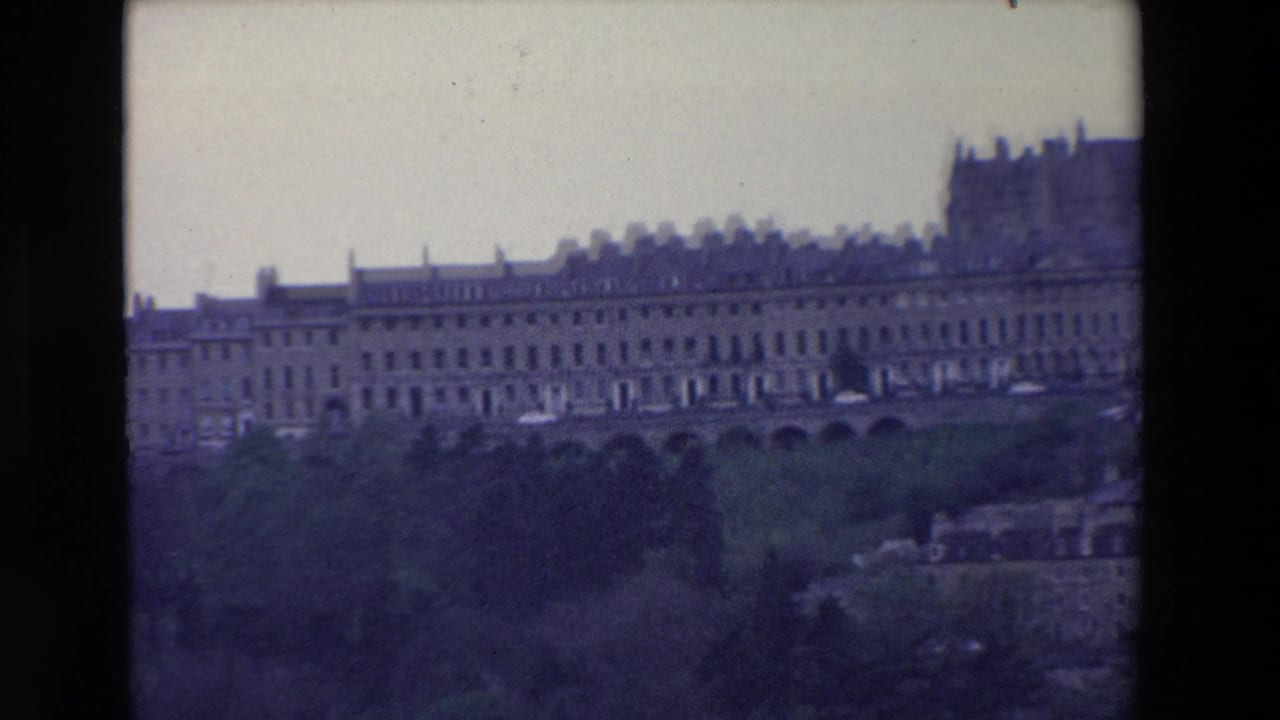 1969 Ireland home-movie view of an extended historic facade with rows of windows, set above a dark wooded slope and partly divided by the film frame edge.