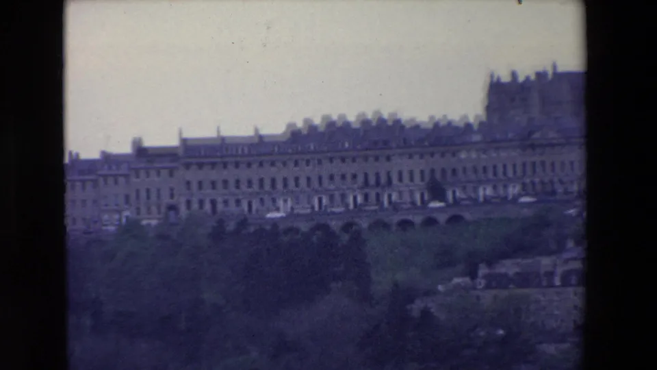 1969 Ireland home-movie view of an extended historic facade with rows of windows, set above a dark wooded slope and partly divided by the film frame edge.