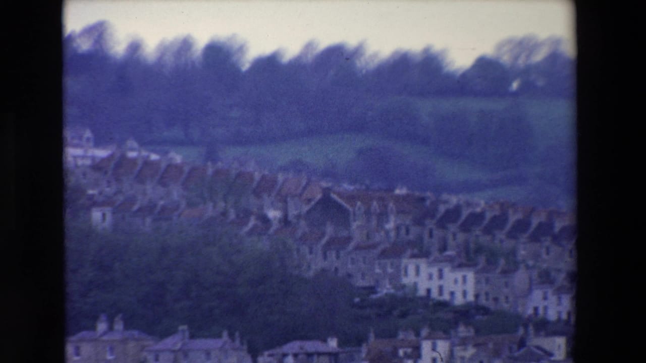 Terraced houses on a hillside with fields and trees behind them.