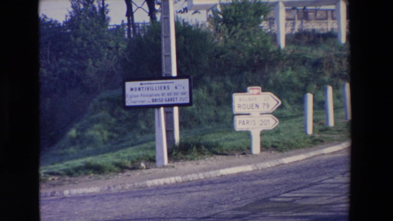 French roadside signs point toward Rouen and Paris near a grassy embankment.