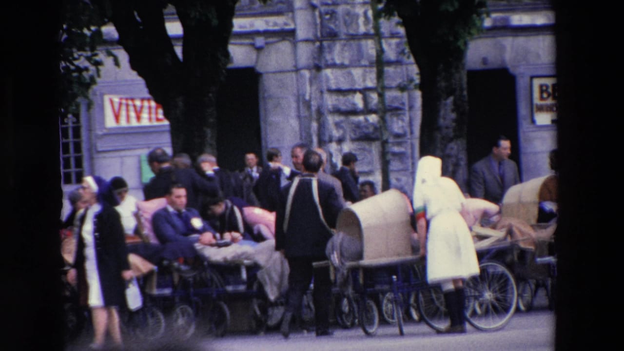Attendants and visitors stand among wheeled chairs and prams near a stone building.