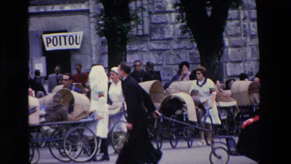In Lourdes, France, according to the clip metadata, nuns and attendants move covered wheeled carts carrying elderly or infirm pilgrims along a stone-walled street in 1969.