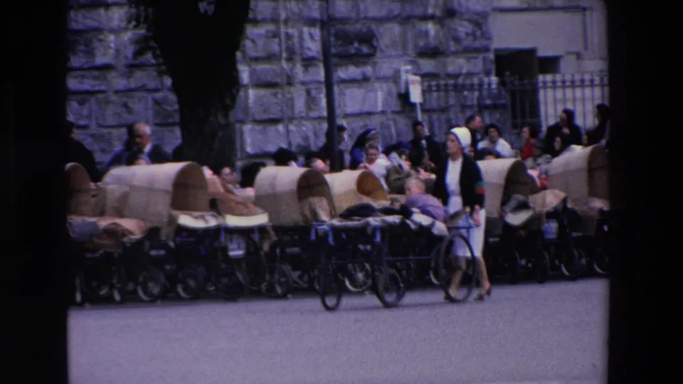 The final frame shows multiple covered carts lined along a Lourdes street with nuns, attendants, seated passengers, and onlookers gathered beside a stone building.