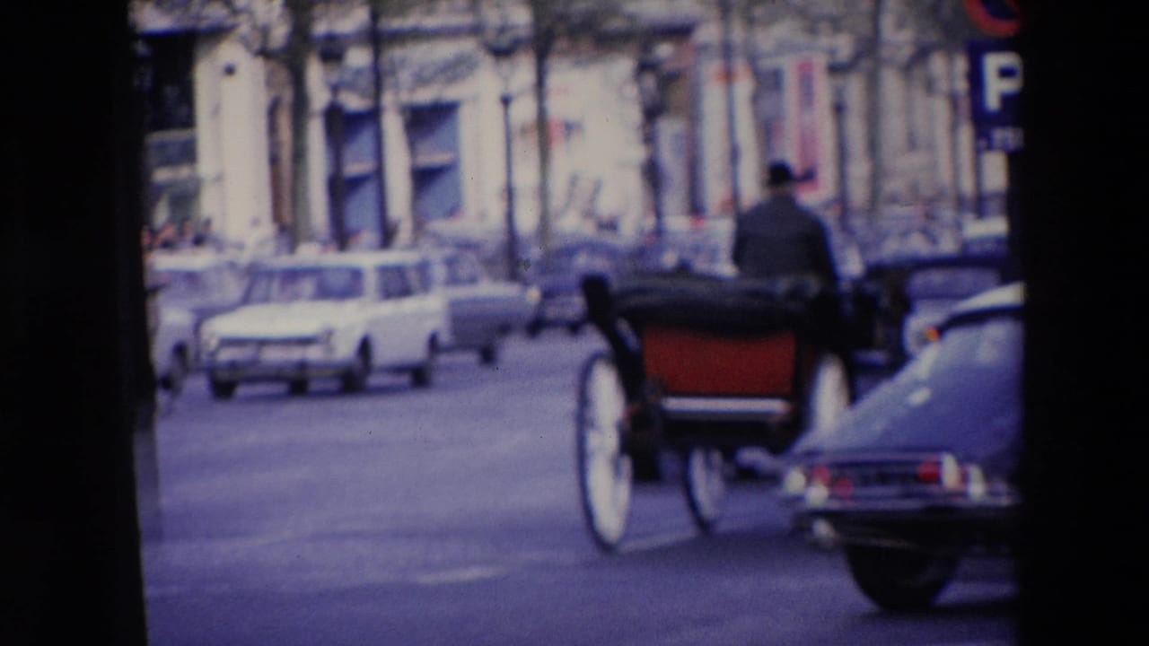 1969 home-movie view in Loudes, France, showing a horse-drawn carriage moving along a street with mid-century cars and stone-fronted buildings.