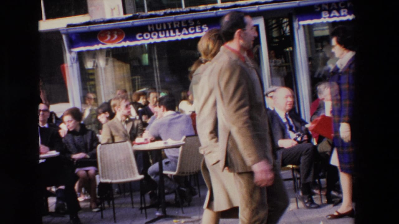 Pedestrians walk past crowded outdoor cafe tables beside a storefront awning.