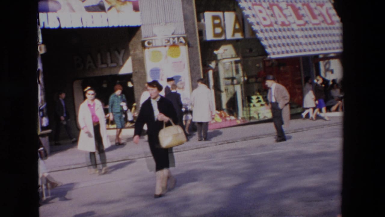 Two women walk across the street in front of Bally and cinema storefronts.