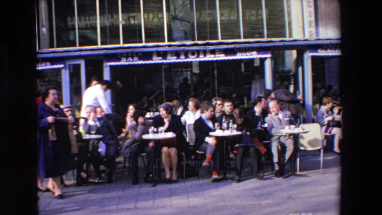 Outdoor cafe scene in Loudes, France with adults seated at small tables, bottled drinks, pedestrians at the edge of frame, and visible L'ETOILE snack bar signage.