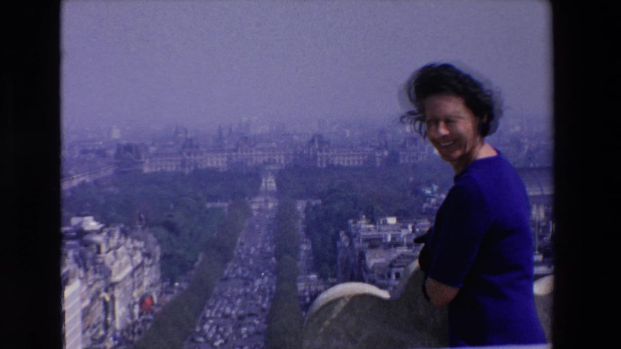 Smiling woman in blue stands at a high rooftop viewpoint over the city.