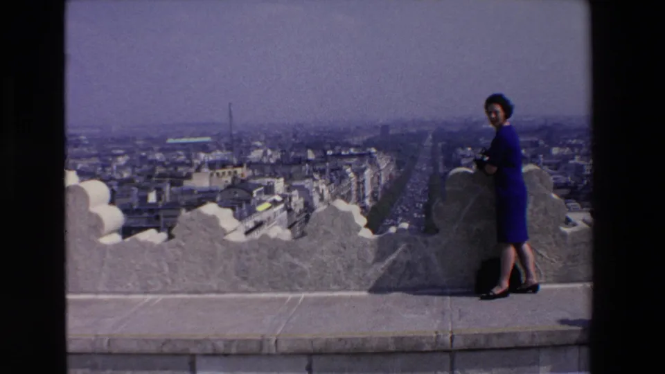 A wide 8mm frame shows the woman standing at the edge of a stone observation deck, with the hazy city and long avenue filling the background.
