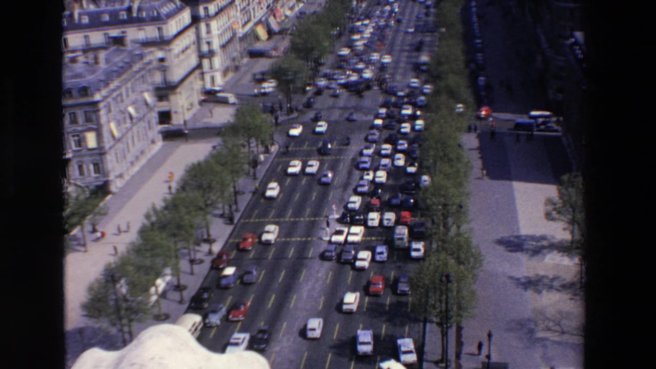 High-angle street view with many cars stopped along a boulevard beside older buildings.
