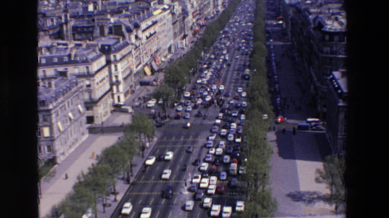 Overhead 1969 France street view showing heavy traffic on a broad tree-lined boulevard bordered by older city buildings and sidewalks.