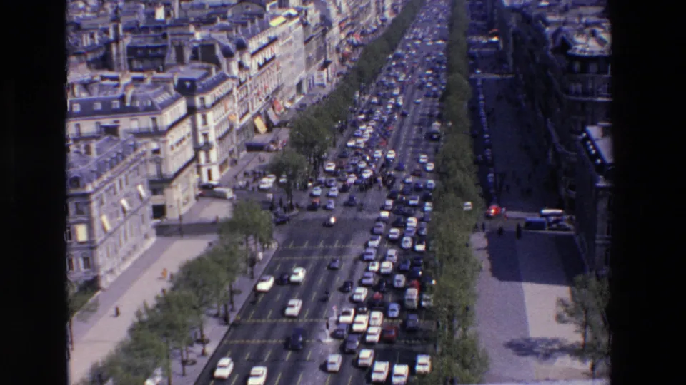 Overhead 1969 France street view showing heavy traffic on a broad tree-lined boulevard bordered by older city buildings and sidewalks.