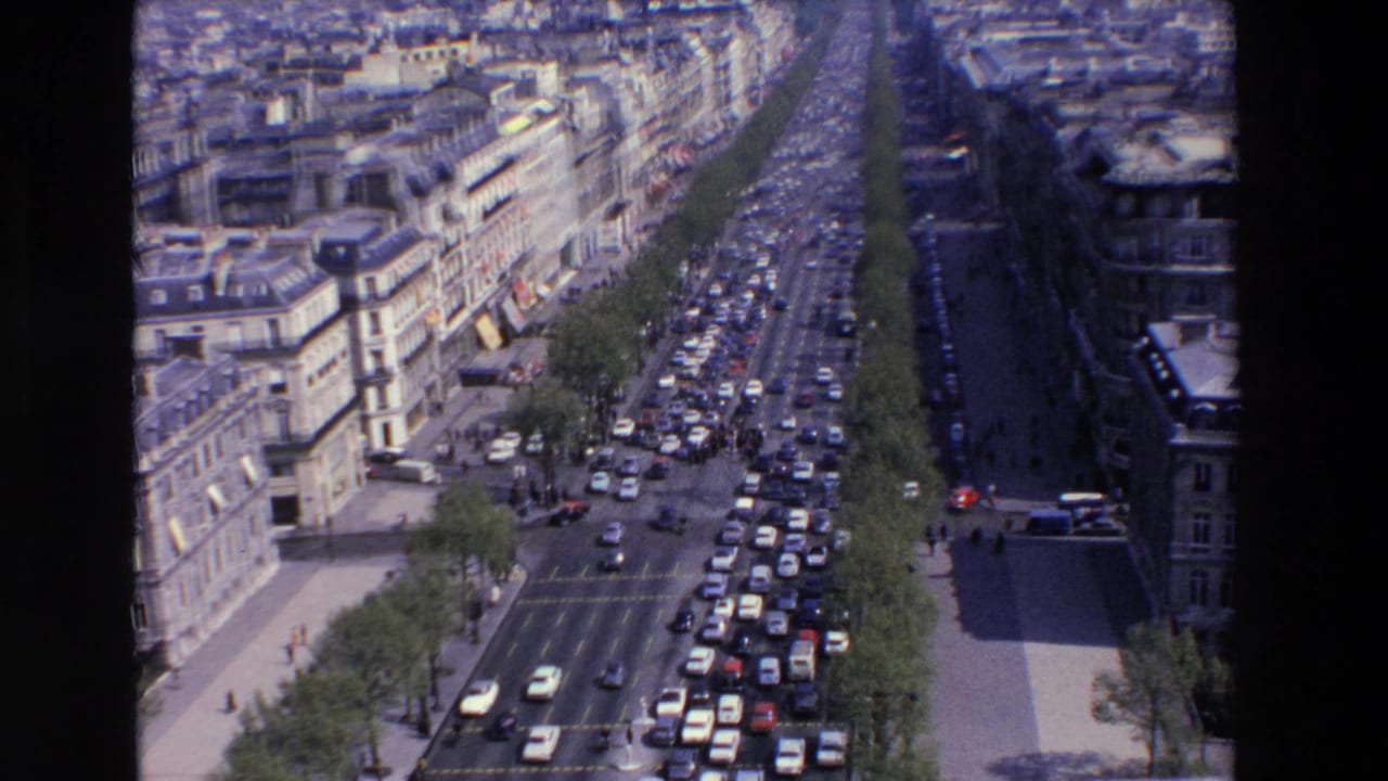 Elevated view of late-1960s city traffic in France, with rows of cars moving along a tree-lined boulevard beside ornate urban buildings.