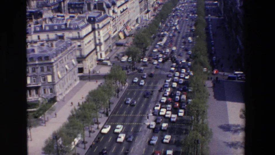 Late-1960s elevated street view in France showing slow-moving cars packed along a broad boulevard with trees, sidewalks, and older city architecture.
