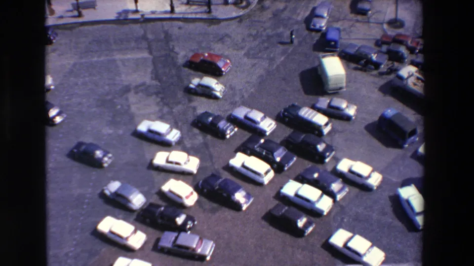 High-angle 1969 Lourdes, France view of many cars dispersed across a broad paved traffic space, suggesting a busy roundabout or intersection area.