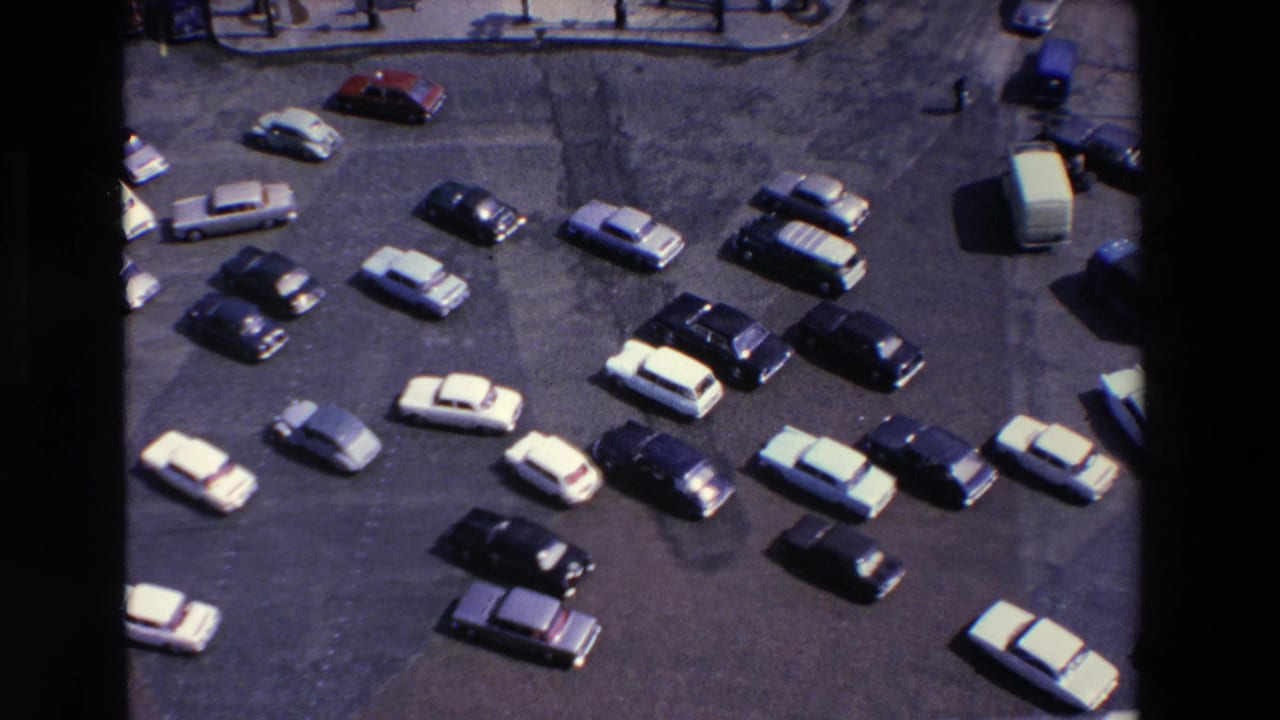 Overhead parking lot view with many light and dark cars arranged in rows.