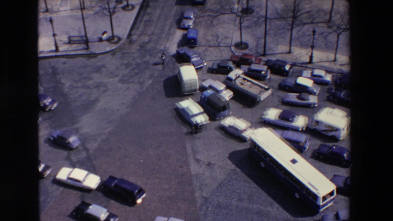 High-angle 1969 8mm view of a crowded French street intersection with many cars, vans, and a long bus moving through traffic.