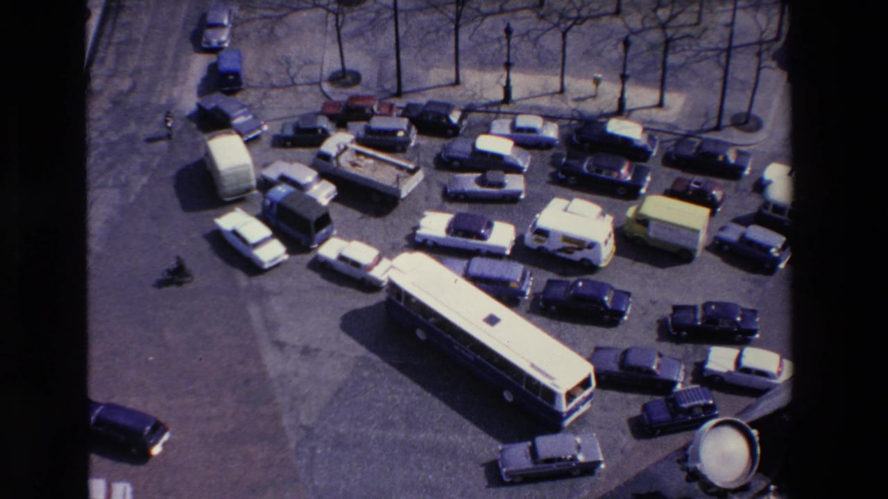 Dense traffic surrounds a long bus near parked cars and vans.