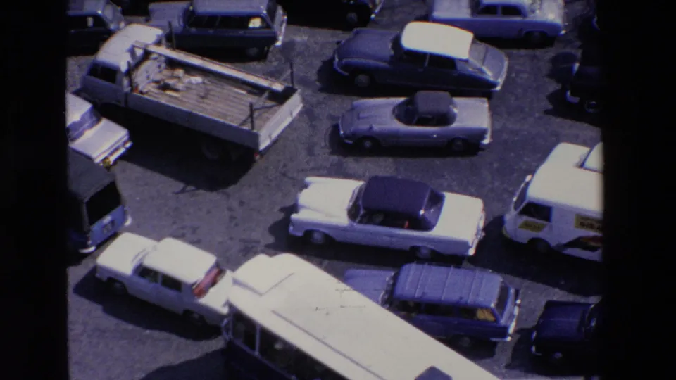 Closer high-angle frame from the 1969 France clip showing the roof of a bus, several compact cars, a light truck, and tightly spaced vehicles in congestion.