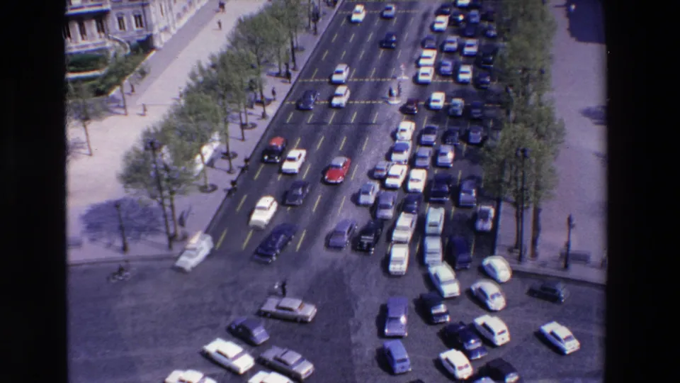 High-angle 1969 France street view showing dense car traffic, pedestrians, tree-lined sidewalks, and ornate building facades at a broad urban intersection.