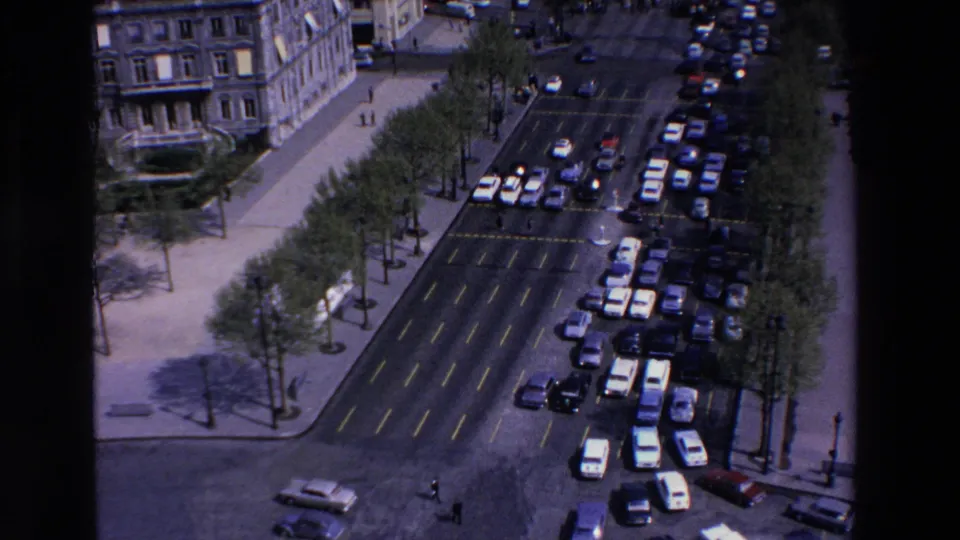 The elevated 8mm view looks down over a French urban avenue in 1969, with many cars, planted sidewalks, and pedestrians near formal stone buildings.