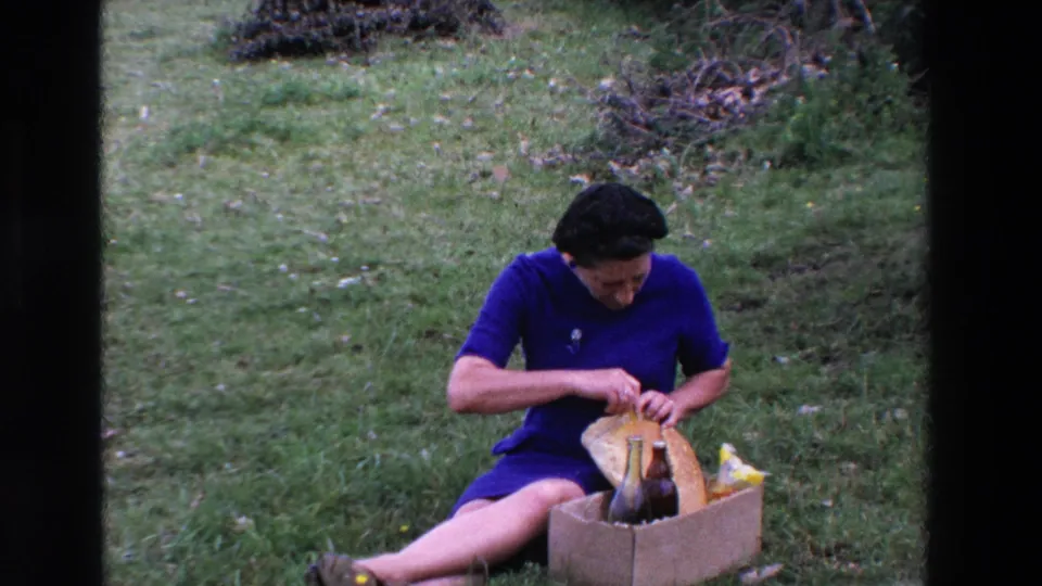 At the end of the short 1969 France clip, the woman continues opening the loaf while seated on the grass beside a cardboard picnic box with dark glass bottles.