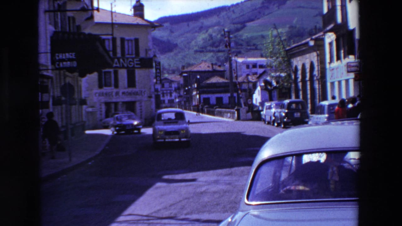 Town street with vintage cars, hillside, and French signage.