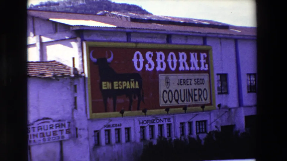 1969 Lourdes, France 8mm frame showing a large red Osborne sign on a white building, with a black bull silhouette, EN ESPAÑA text, and JEREZ SECO COQUINERO branding.