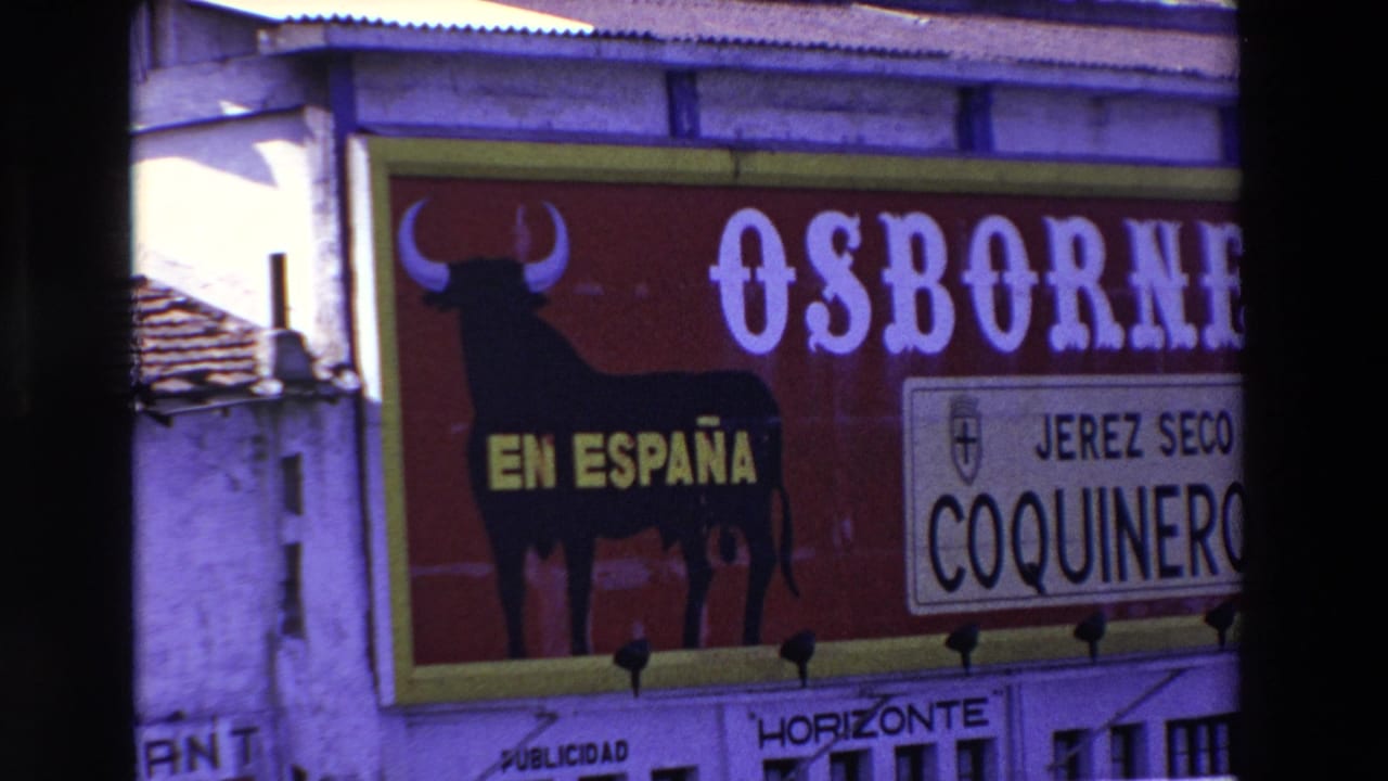 1969 8mm frame showing a large red Spanish-language Osborne billboard with a black bull silhouette, yellow EN ESPAÑA text, and a smaller Jerez Seco Coquinero panel beside building edges.