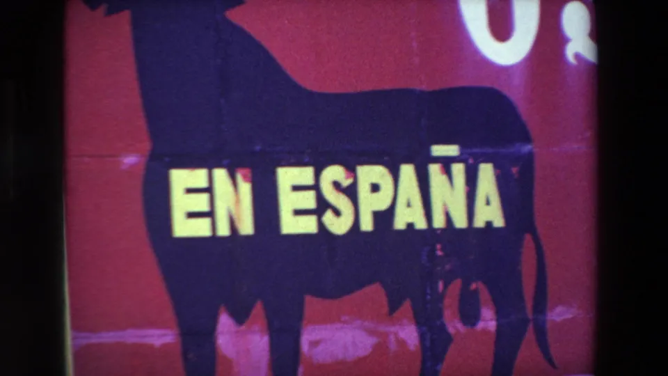 1969 8mm close framing of the bull silhouette, yellow EN ESPAÑA text, red painted billboard surface, and partial white lettering near the top edge.