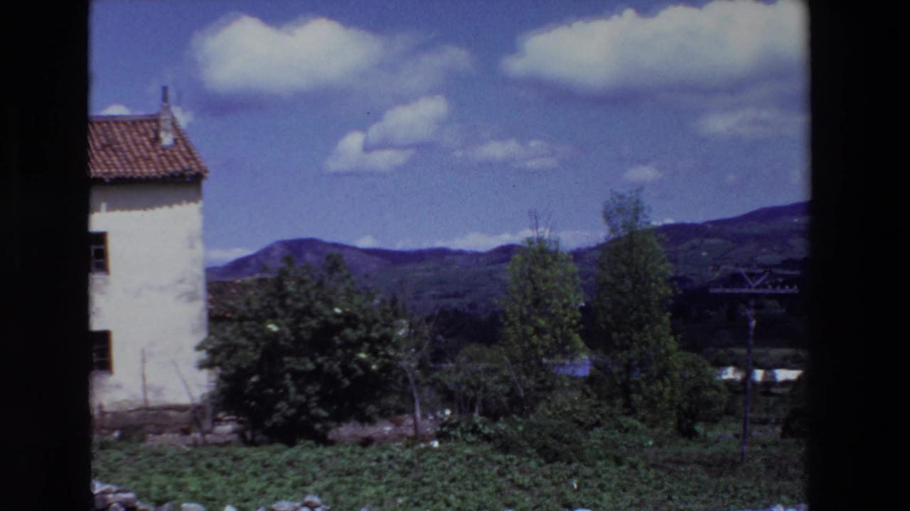 Partial side view of the white house with valley vegetation, hills, and a utility pole nearby.