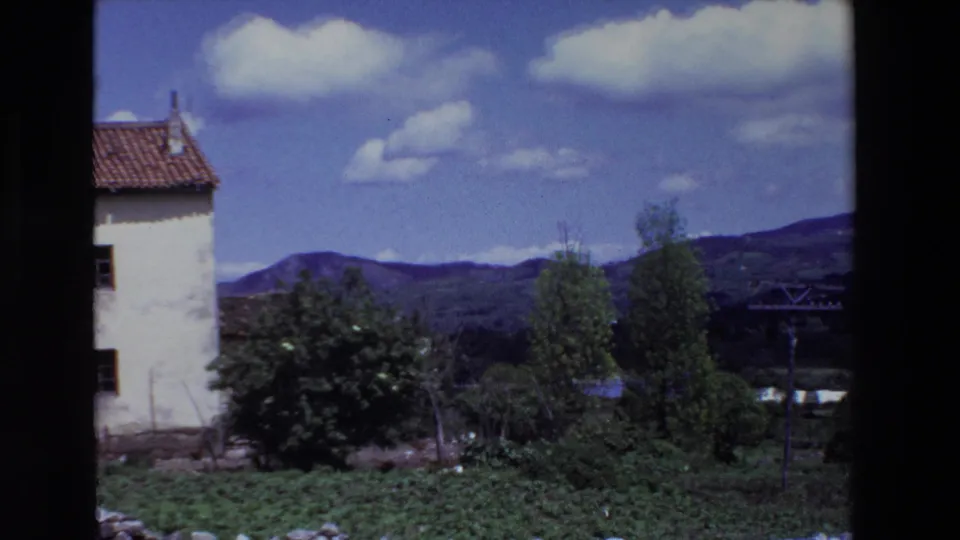1969 Lourdes, France 8mm frame during the pan, with the white house partly cut off at left, a red tile roof, green valley growth, distant hills, and a utility pole at right.