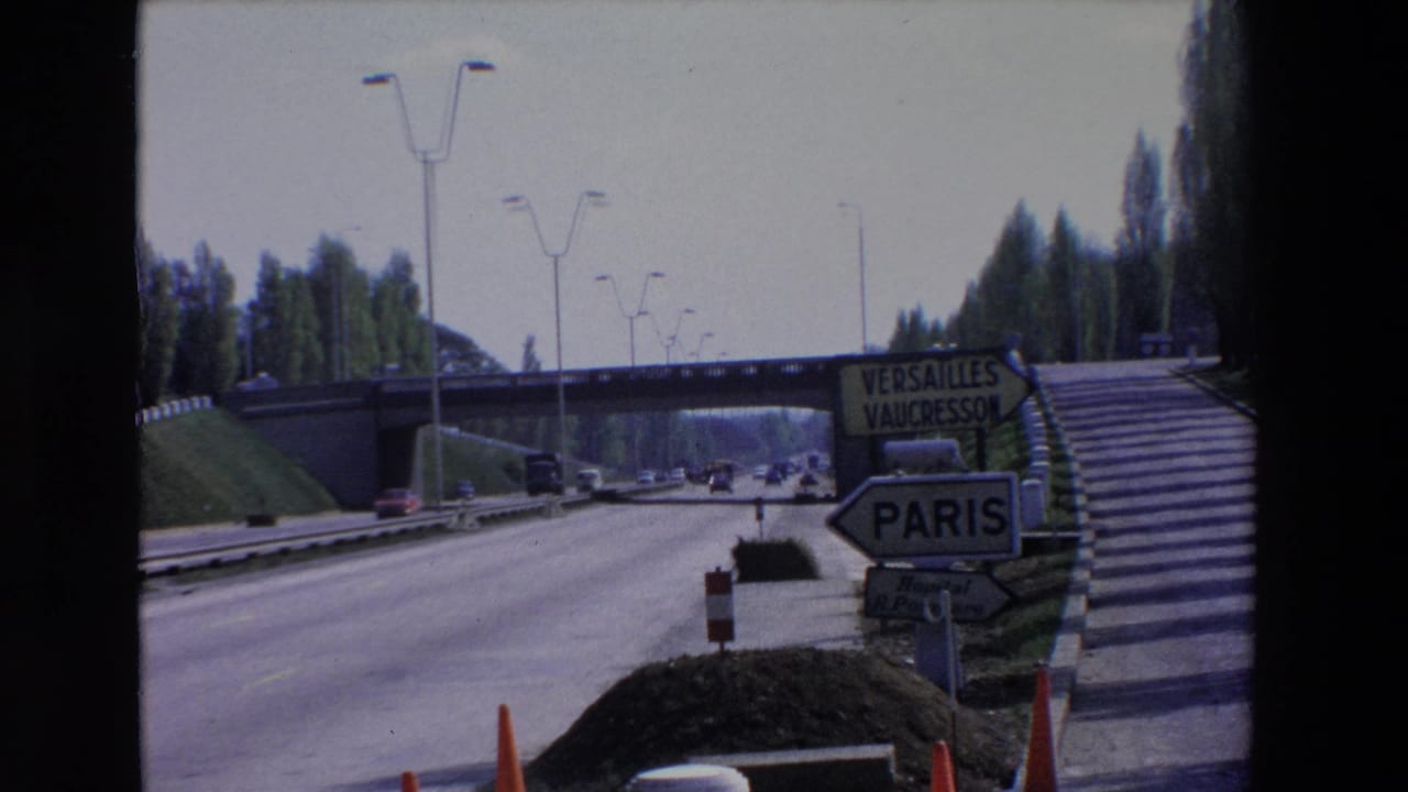 Paris-area roadside view with highway lanes, cars, a pedestrian-style stair embankment, and signs indicating Paris, Versailles, and Vaucresson.