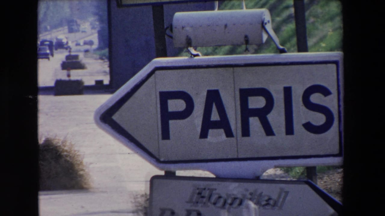 Close 8mm frame of a Paris directional sign on a French roadway, with cars and roadside greenery visible beyond the sign.