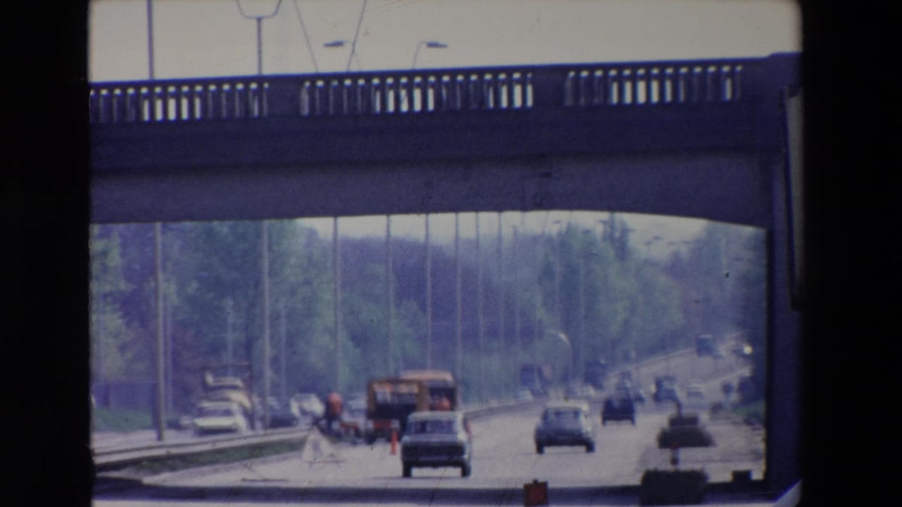 Traffic approaches roadwork markers under an overpass on a tree-lined road.