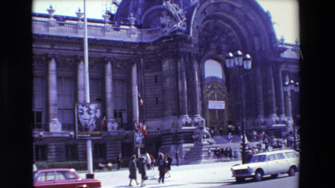 Closer angled view of the building entrance with pedestrians, red car, poster, and stone columns.