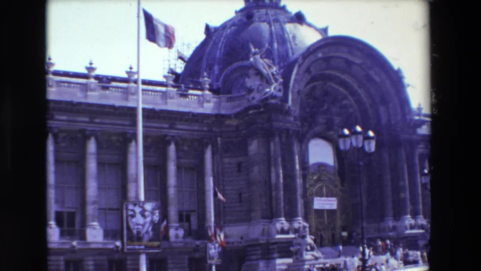 1969 Paris 8mm frame showing a French flag at half-mast before a grand domed Beaux-Arts building with columns, scaffolding, a streetlamp, a poster, and small pedestrians.