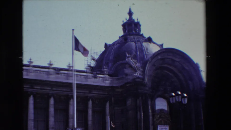 1969 Paris frame showing the flagpole with the French flag at half-mast in front of a domed classical building, with scaffolding, roofline detail, columns, and a streetlamp visible.