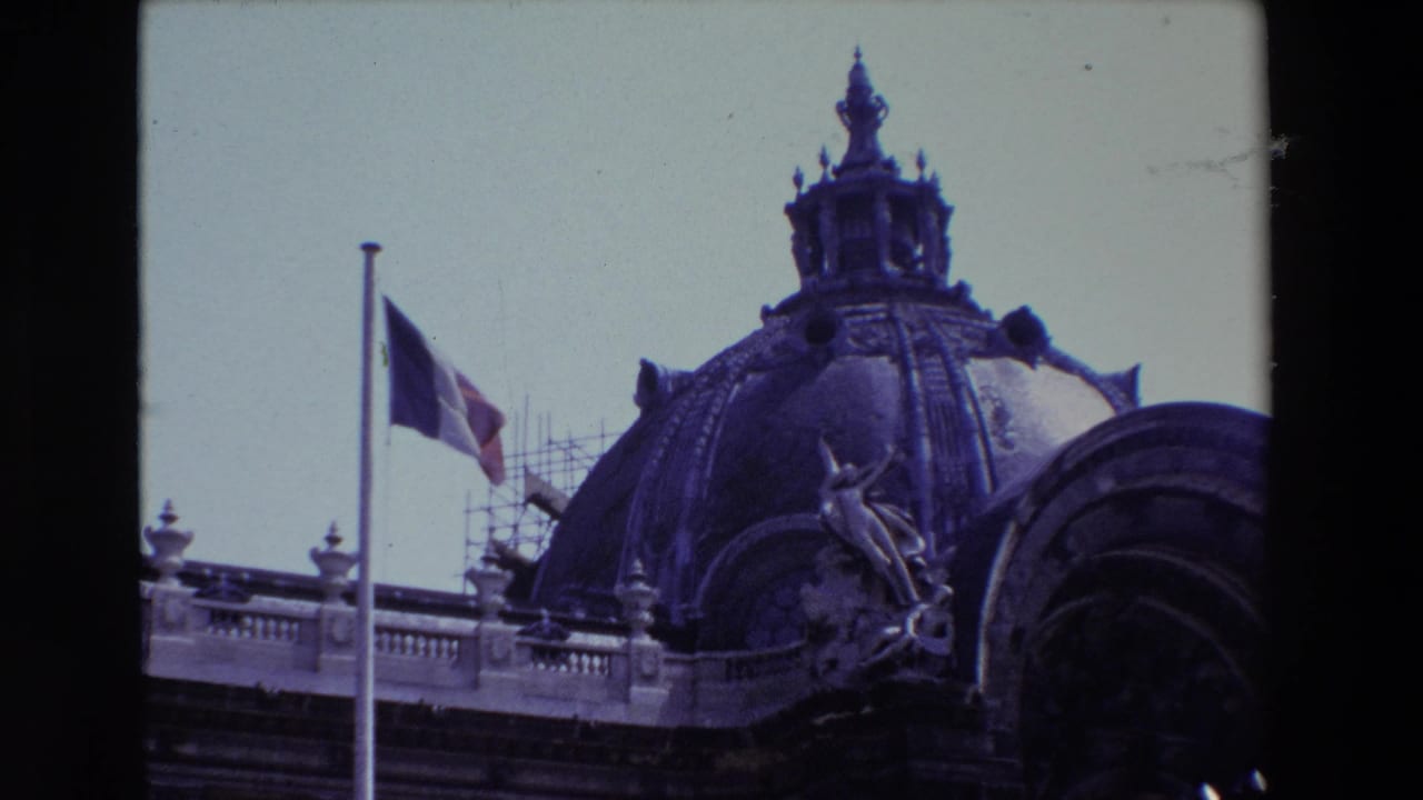1969 Paris 8mm frame with a closer view of a decorated dome, French flag, roof balustrade, and scaffolding on the historic building exterior.