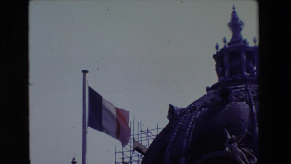 1969 Paris 8mm frame tightly framing the French flag at half-mast, repair scaffolding, and the right edge of an ornate domed building.