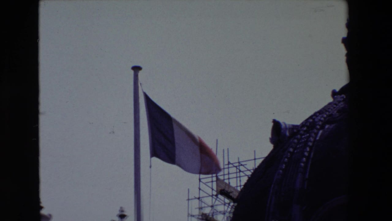 A French tricolor flag waves on a tall pole near ornate Paris architecture and scaffolding in 1969 home-movie footage.