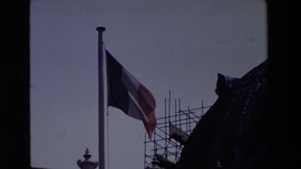 A visitor-shot 1969 Paris frame shows the French flag waving near scaffolding, with ornate architectural detail partly silhouetted at the side.